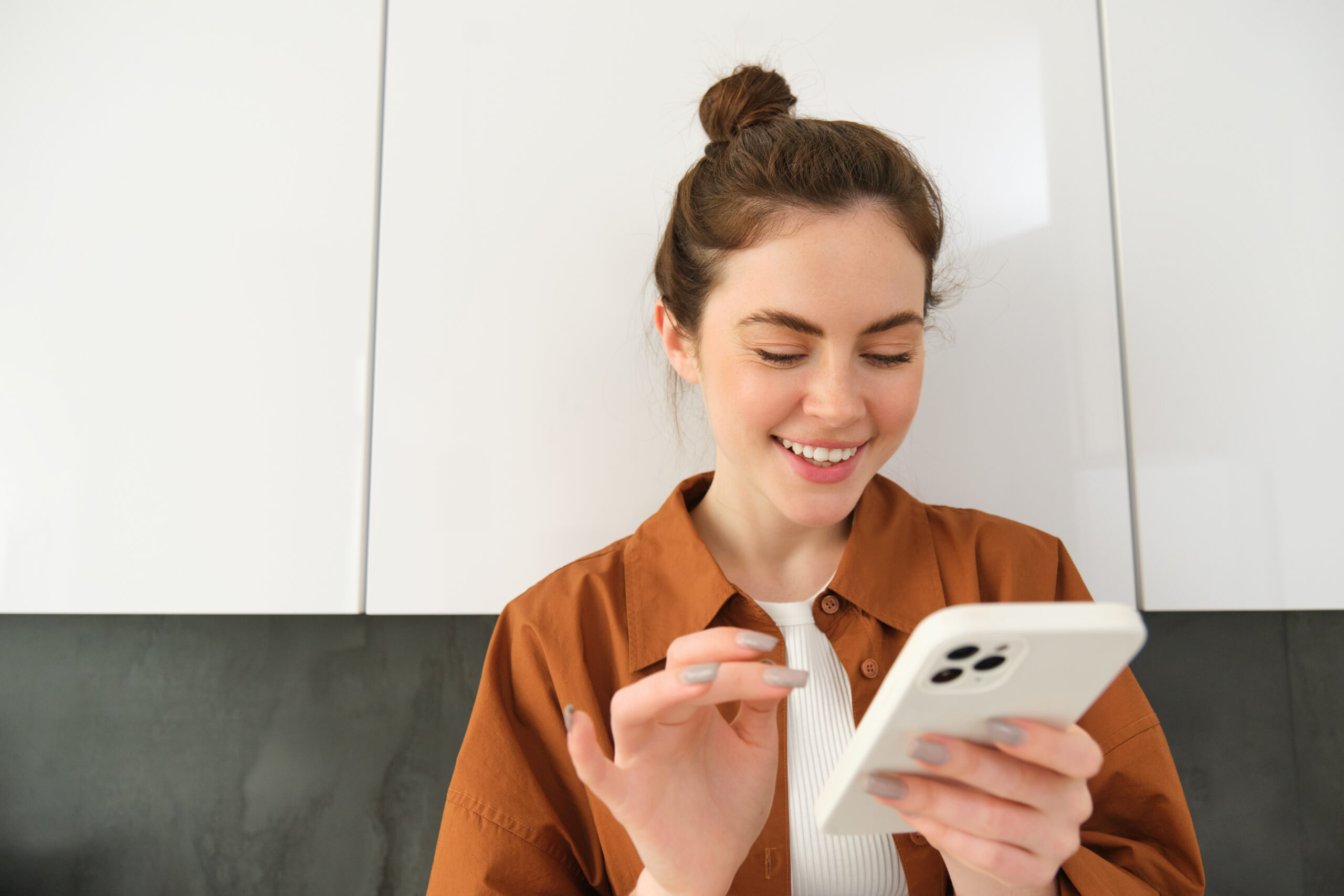Happy girl with smartphone, looking at phone and smiling, standing at home, concept of buying online, shopping in mobile app.