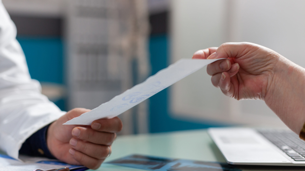 Physician giving prescription document to patient in cabinet, after medical consultation. Medic holding checkup report to give treatment to retired person in health care office. Close up